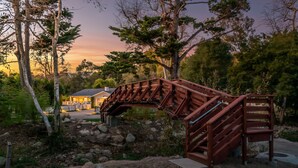 A wooden bridge in a natural setting with a house in the background. - Casa Miramar - Coastal Farmhouse Chic Getaway (Santa Barbara)