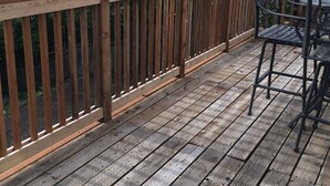 Een houten terras met een metalen reling, tafel en stoel.
