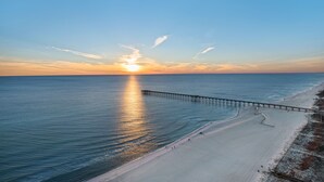 A beach with a pier extending into the water, a clear sky, and the sun setting or rising.