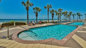 A swimming pool with a view of the ocean, surrounded by palm trees and lounge chairs.
