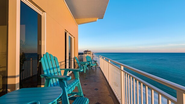 A balcony with turquoise Adirondack chairs and a table, overlooking the ocean.