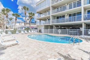 A hotel with a swimming pool, multiple balconies, and palm trees.