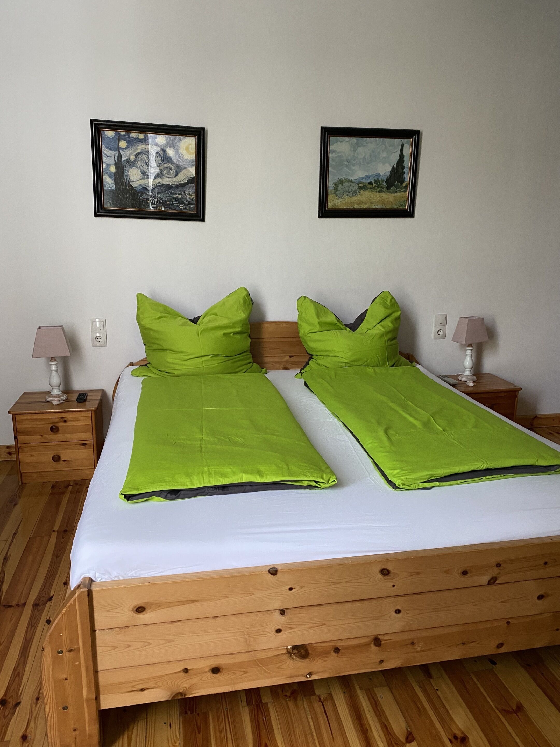 Un letto matrimoniale con biancheria verde, due comodini con lampade e due quadri appesi al muro.