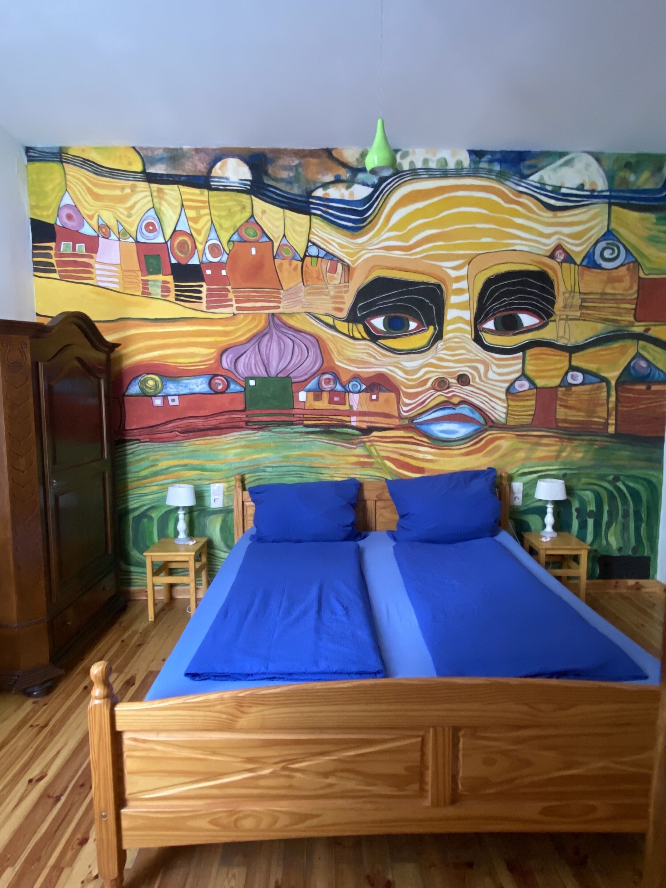 Une chambre avec un lit, deux tables de chevet et une tapisserie colorée au mur.