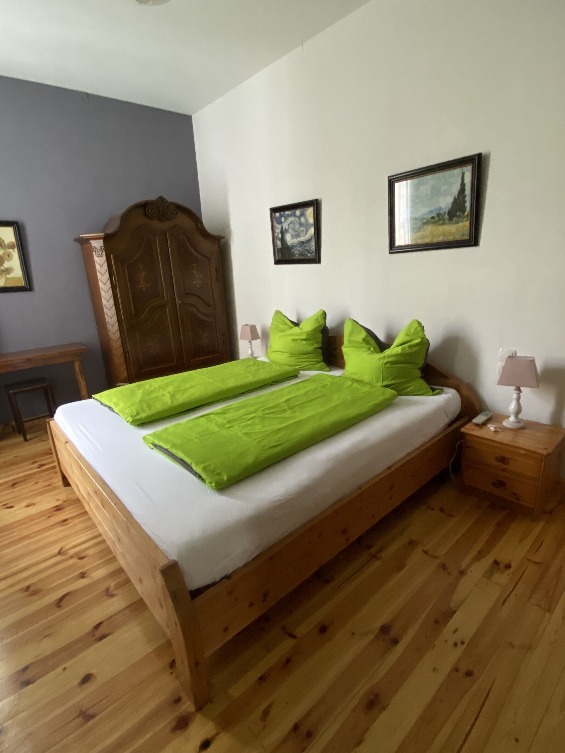 Una camera da letto con un letto in legno, cuscini verdi, un comodino in legno, una lampada e due quadri appesi al muro.