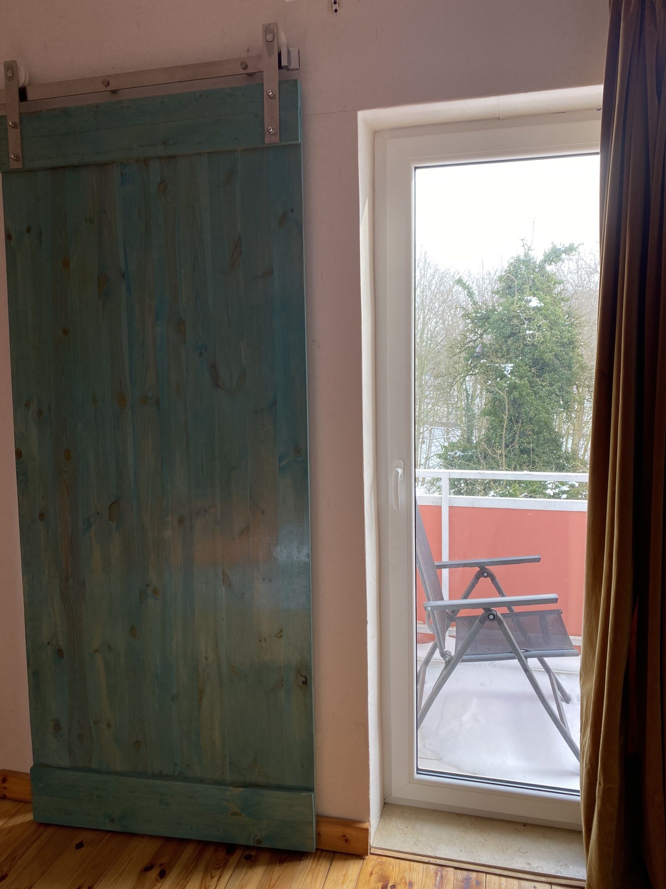 Une pièce dotée d’une grande fenêtre, d’une porte coulissante et donnant sur un balcon aménagé avec du mobilier d’extérieur.