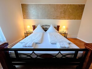 A neatly made bed with white linens and pillows, two bedside tables with lamps, and a headboard with a geometric design. - Hafen12 (Bremerhaven)