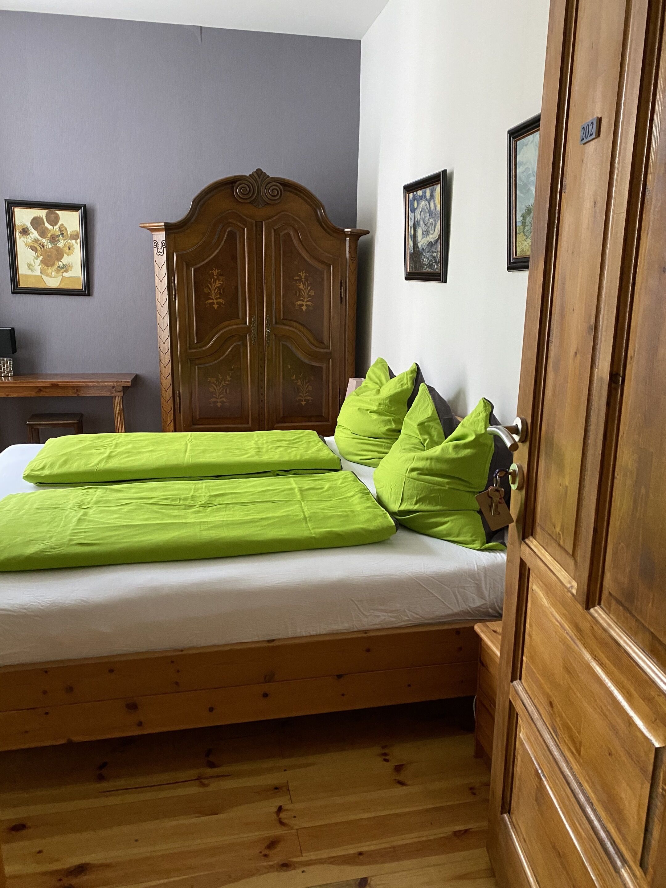 A bedroom with a wooden bed, green bedding, a wooden wardrobe, and a small desk.