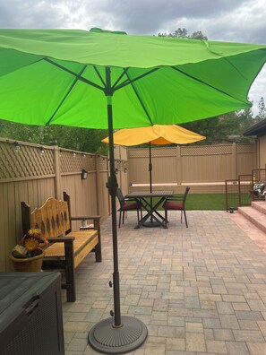 A patio with a table and chairs, a wooden bench, and a green umbrella.