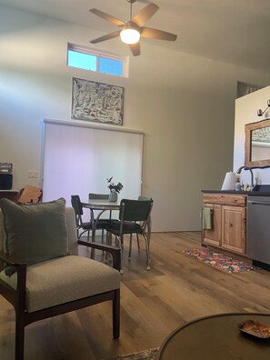 A dining area with a table and chairs, a ceiling fan, a window with blinds, and a kitchen area with a refrigerator and cabinets.