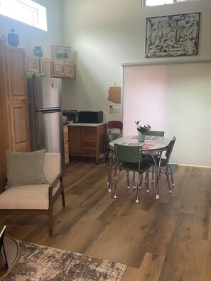Ein Essbereich mit einem runden Tisch, Stühlen, einem Holzschrank, einem Kühlschrank und einer Mikrowelle.