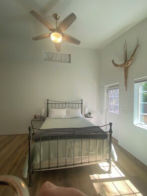 A bedroom with a bed, a ceiling fan, a window, and a wall-mounted deer head decoration.