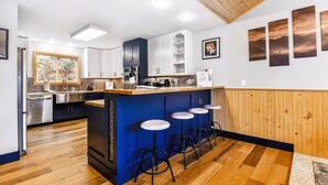 Cozinha moderna com ilha azul e banquetas, piso de madeira e vista para o exterior através de uma janela.