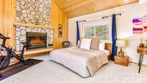 Quarto com lareira de pedra, teto de madeira e cama com vista para o exterior.