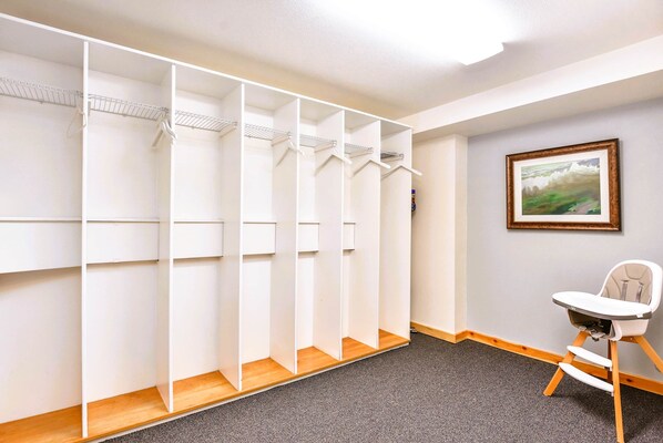 A walk-in closet with multiple shelves and hanging space, a wooden floor, and a baby high chair in the corner.