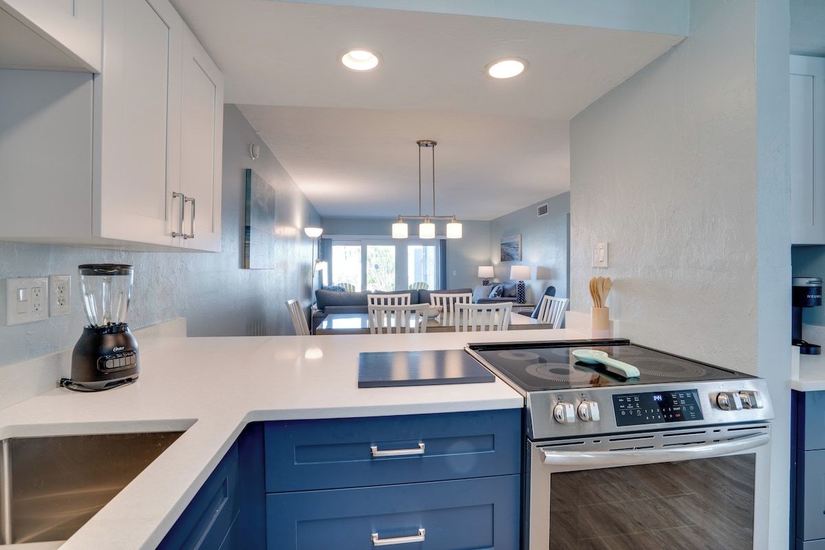 A modern kitchen with a built-in stove, a blender, and a dining area with a table and chairs.