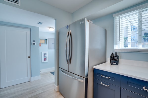 A modern kitchen with a stainless steel refrigerator, a white countertop, and a window with blinds.