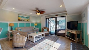 A living room with a sofa, two wicker chairs, a coffee table, a TV stand, and a ceiling fan. - Pool! First row from beach front with 2 Private Balconies (Carolina Beach)