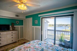A bedroom with a bed, dresser, ceiling fan, and a view of a water body through a sliding glass door. - Pool! First row from beach front with 2 Private Balconies (Carolina Beach)