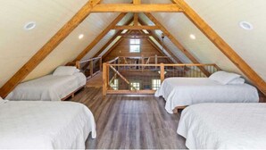 A triangular attic bedroom with wooden beams, a lofted sleeping area, and a staircase. - Quiet Escape from the City (Fitzpatrick)