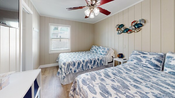 A bedroom with two beds, a ceiling fan, a window with blinds, and a wall decoration of fish.