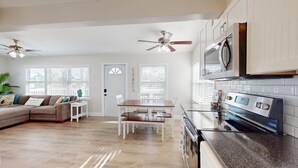 A spacious living area with a wooden floor, a dining table with chairs, a sofa, and a ceiling fan.