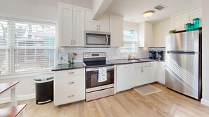 A modern kitchen with white cabinetry, a stainless steel refrigerator, a microwave, and a built-in oven.