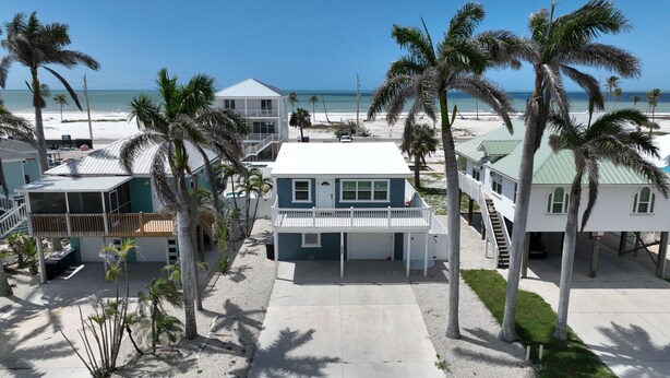 A beachfront property with multiple buildings, including a two-story house with a balcony, a smaller structure with a covered porch, and a building with a green roof.