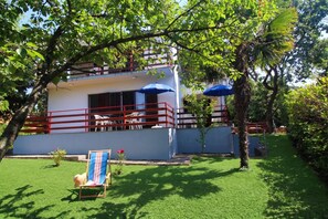 A two-story building with a balcony, surrounded by lush greenery and a well-maintained lawn.