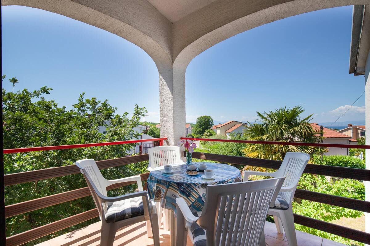 A balcony with a round table, white chairs, and a red railing.