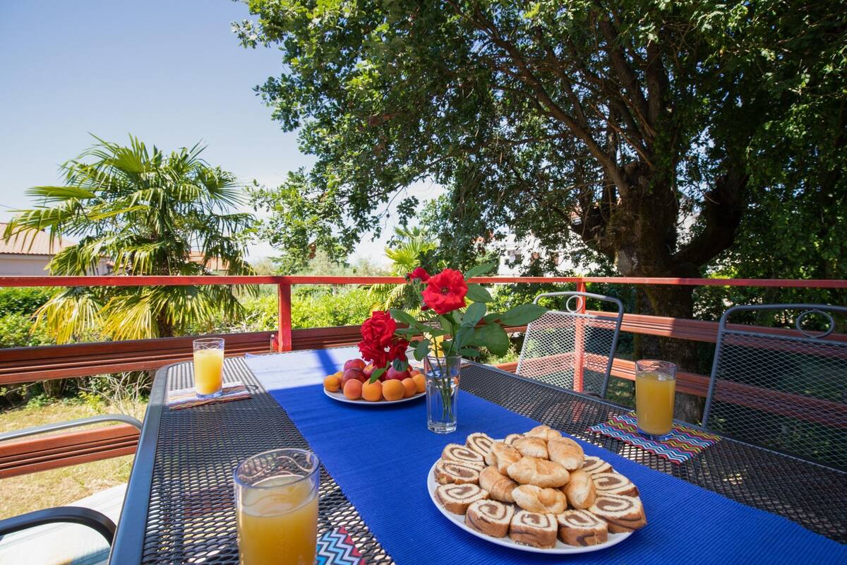 An outdoor dining area with a table set for breakfast, including pastries, fruit, and drinks.