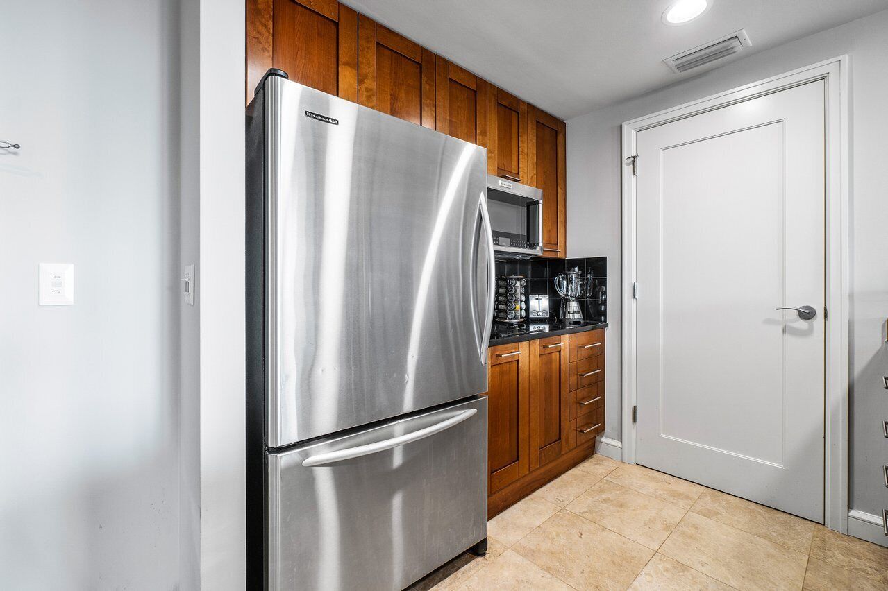 A kitchen with a stainless steel refrigerator, wooden cabinets, a microwave, and a white door.