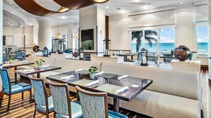 Una moderna hall d'albergo con un'area salotto centrale, una reception e ampie finestre che si affacciano sull'oceano.