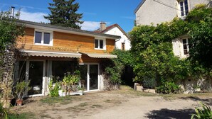 Ein zweigeschossiges Haus mit Holzfassade, einer Veranda und einem Gartenbereich mit Topfpflanzen.
