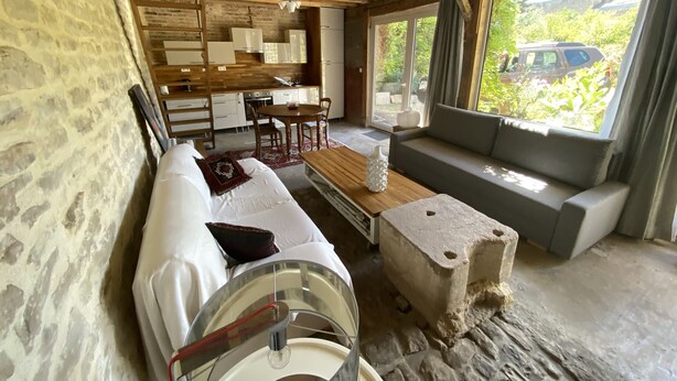 Ein rustikales Blockhaus-Interieur mit einer Steinwand, Holzbalkendecke, einer Couch, einem Esstisch und einer Küchenzeile.