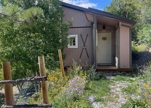 A small cabin with a door, a window, and a wooden fence in front.