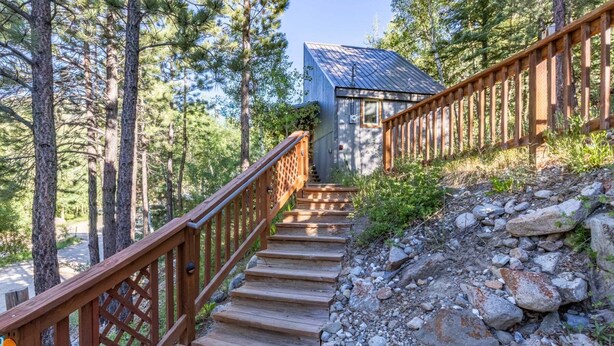 A wooden staircase leading to a cabin with a metal roof, surrounded by trees.