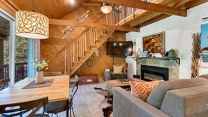 A wooden interior with a dining table, sofa, fireplace, and staircase.