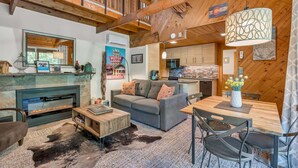A cozy living room with a fireplace, a sofa, a dining table, and a kitchen area.