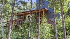 A cabin with a wooden deck, surrounded by tall trees.