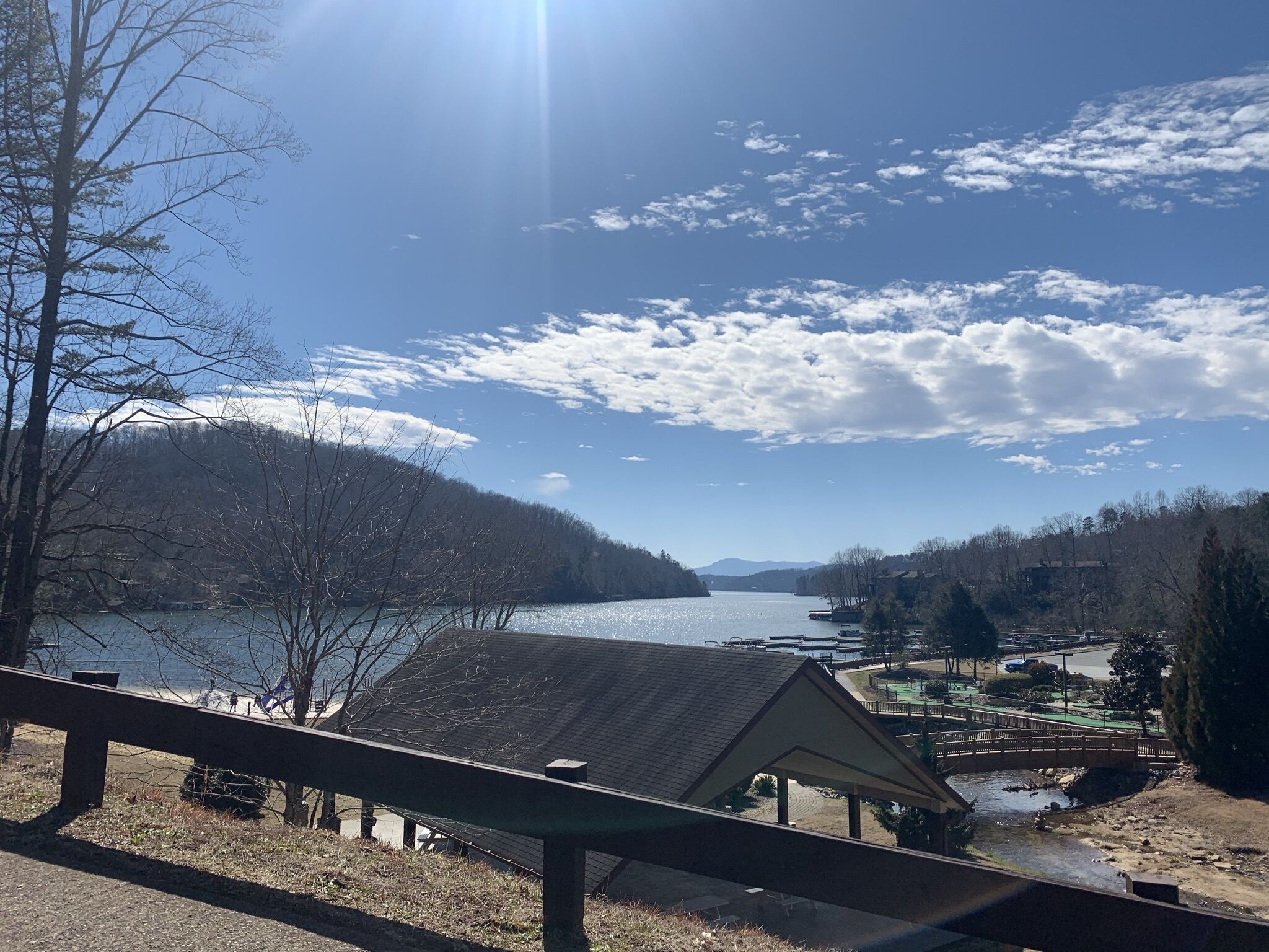 Vista su un lago con un ponte di legno, un piccolo padiglione e una catena montuosa in lontananza.