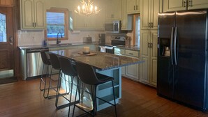Una cocina con una isla central, taburetes de bar, electrodomésticos de acero inoxidable y una araña.