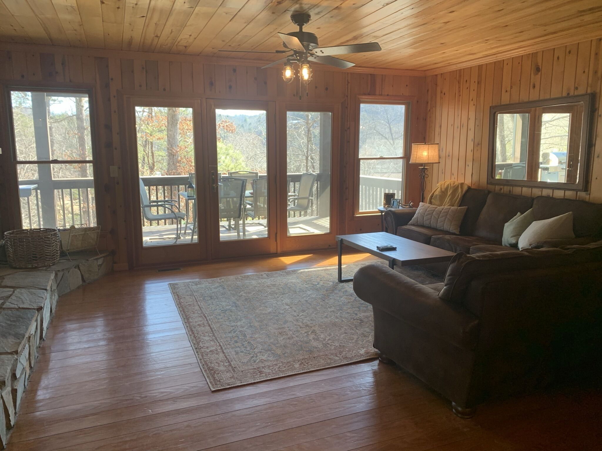 A wooden interior with a sofa, coffee table, and a view through large glass doors to an outdoor deck.