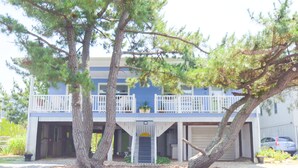 A two-story house with a balcony, garage, and large trees in front. - Beach home nestled between the beach and the bay (eastside) (Bethany Beach)