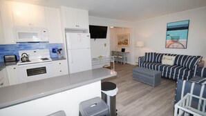 A modern kitchen with white cabinets, a microwave, and a stove. There is a dining area with a table and chairs, and a living room with striped furniture and a painting of a bicycle. - Beach home nestled between the beach and the bay (eastside) (Bethany Beach)