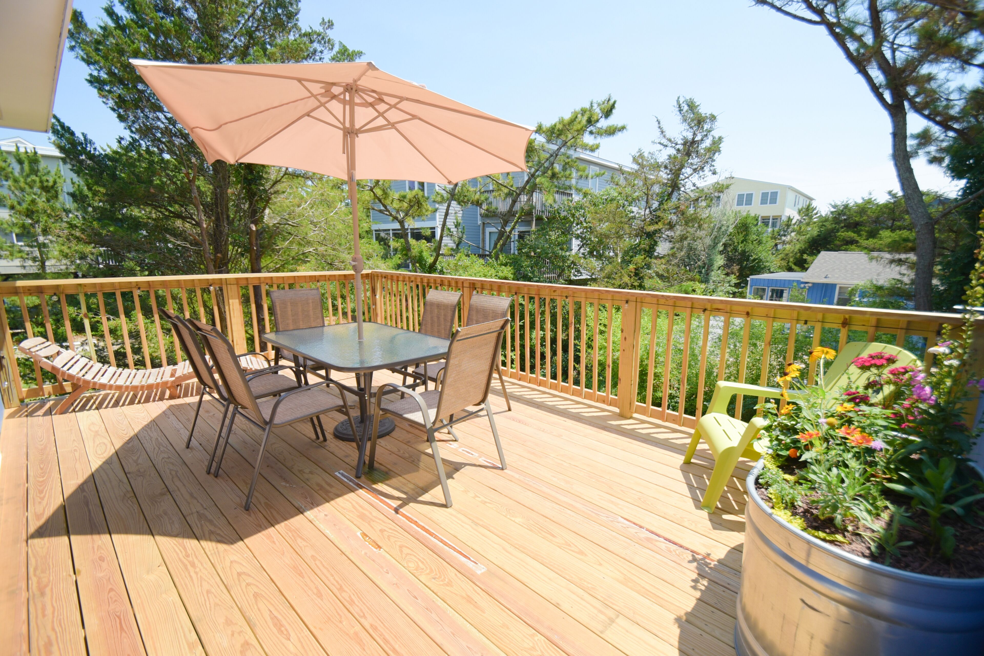 A wooden deck with a table and chairs, a large umbrella, and a planter with flowers.