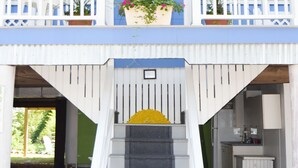 A two-story building with a blue exterior, white railings, and a central staircase leading to a balcony with potted plants. - Beach home nestled between the beach and the bay (eastside) (Bethany Beach)