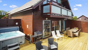 Eine Holzterrasse mit Gartenmöbeln, einem Whirlpool und einem Grill.
