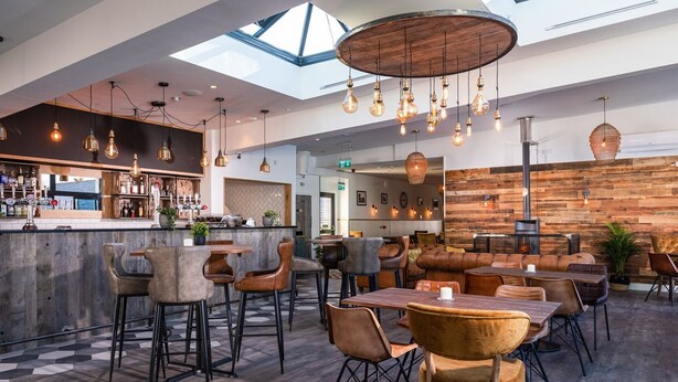 Ein modernes Restaurant mit Barbereich, Holzwänden und verschiedenen Sitzgelegenheiten, darunter Barhocker und gepolsterte Stühle.