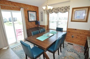 A dining area with a wooden table, blue chairs, a chandelier, and a view through the window. - 472 Pool,HotTub,Elevator,OceanViews,DogFriendly (Nags Head)